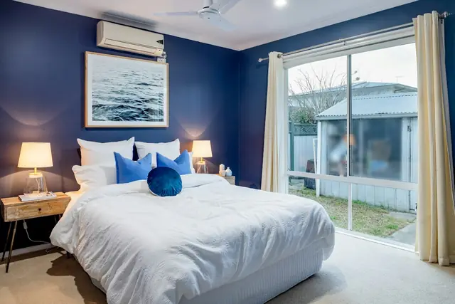 Quarto claro de paredes azul-escuras com um split branco instalado acima da cabeceira da cama